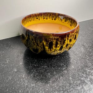 May include: A yellow and brown ceramic bowl with a speckled glaze. The bowl is round and has a wide rim.