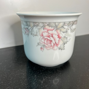 May include: White ceramic planter with a floral design featuring pink and gray roses and leaves.