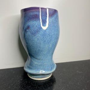 May include: A blue and purple ceramic mug with a white glaze. The mug has a rounded bottom and a wide opening.