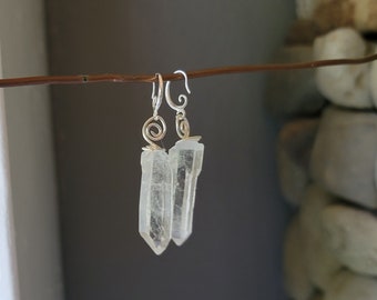 Puede incluir: Un par de pendientes de plata con puntas de cristal de cuarzo transparente. Los cristales están envueltos en alambre de plata y los pendientes tienen un cierre de gancho simple.