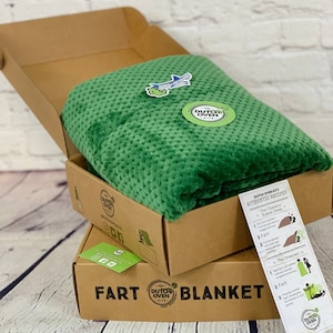 Picture of a fleece throw blanket from Dutch Oven Kits Tactical Green Color close up on  wood floor with a white brick background