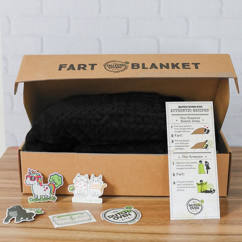 A black blanket in a box sits on a wood and white brick background. Dutch Oven Kits Fart Blanket.