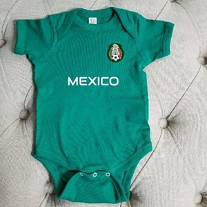 May include: Green baby onesie with a white embroidered Mexican soccer team logo and the word "MEXICO" on the front.