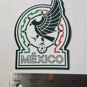 Puede incluir: Un parche bordado con el logotipo del equipo nacional mexicano. El logotipo es blanco con acentos verdes y rojos y representa un águila con las alas extendidas, un balón de fútbol y la palabra "MÉXICO" en letras blancas.