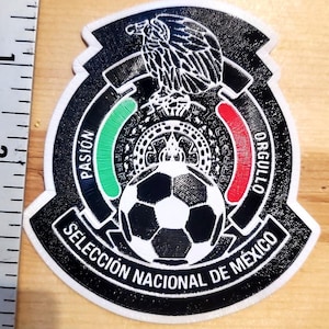 May include: A black, white, green, and red embroidered patch featuring an eagle, a soccer ball, and the text PASIÓN, ORGULLO, and SELECCIÓN NACIONAL DE MÉXICO. A metal ruler is visible on the left, showing a measurement of approximately 1 inch.
