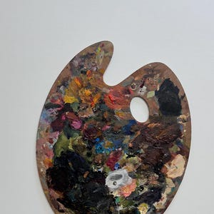 以下が含まれることがあります： 親指用の穴が開いた楕円形の木製アーティストパレット。黒、赤、黄、青、白など、様々な色の乾燥した油絵具が厚く質感豊かに塗り重ねられています。木製の表面の下部には「BEST」という文字が印刷されています。