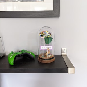 May include: A glass dome with a colorful rose inside. The rose is made of fabric and has a comic book pattern. A small figurine is sitting on a base inside the dome. The base has a small sign that reads "You are my  " and a small sign that reads "  " .