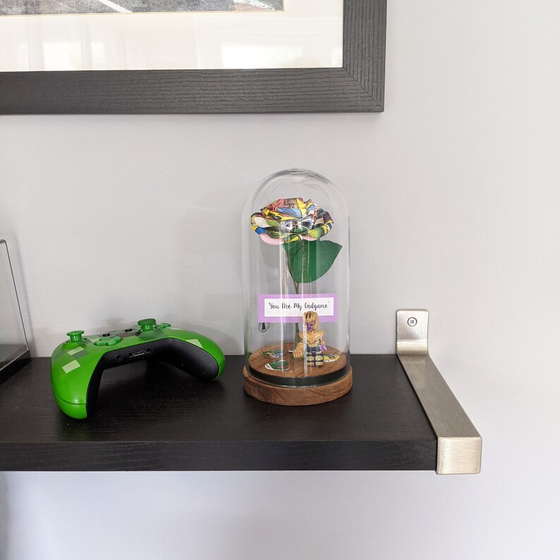 May include: A glass dome with a colorful rose inside. The rose is made of fabric and has a comic book pattern. A small figurine is sitting on a base inside the dome. The base has a small sign that reads "You are my  " and a small sign that reads "  " .
