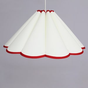 Könnte beinhalten: Ein weißer Lampenschirm mit einem roten, gewellten Rand. Der Lampenschirm ist aus Stoff und hat ein plissiertes Design.