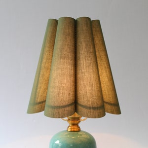 May include: A green fabric lampshade with a pleated design sits atop a teal ceramic lamp base with a gold metal fixture.
