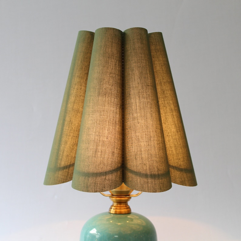 May include: A green fabric lampshade with a pleated design sits atop a teal ceramic lamp base with a gold metal fixture.