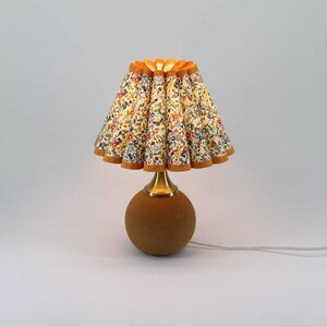 May include: A small table lamp with a floral patterned lampshade. The lampshade is pleated and has a scalloped edge. The base is a brown sphere with a brass-colored neck.