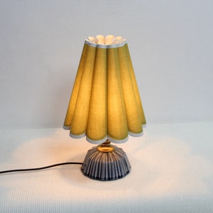 Może przedstawiać: Lampa stołowa z plisowanym, żółtym abażurem i niebiesko-białą podstawą ceramiczną.