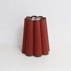 May include: A red lampshade with a brown trim. The lampshade is pleated and has a scalloped edge.
