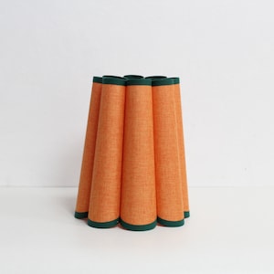May include: Orange lampshade with a green trim. The lampshade is made of a textured fabric and has a pleated design.
