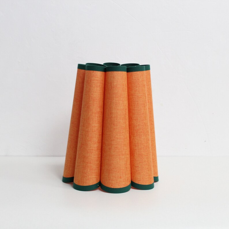 May include: Orange lampshade with a green trim. The lampshade is made of a textured fabric and has a pleated design.