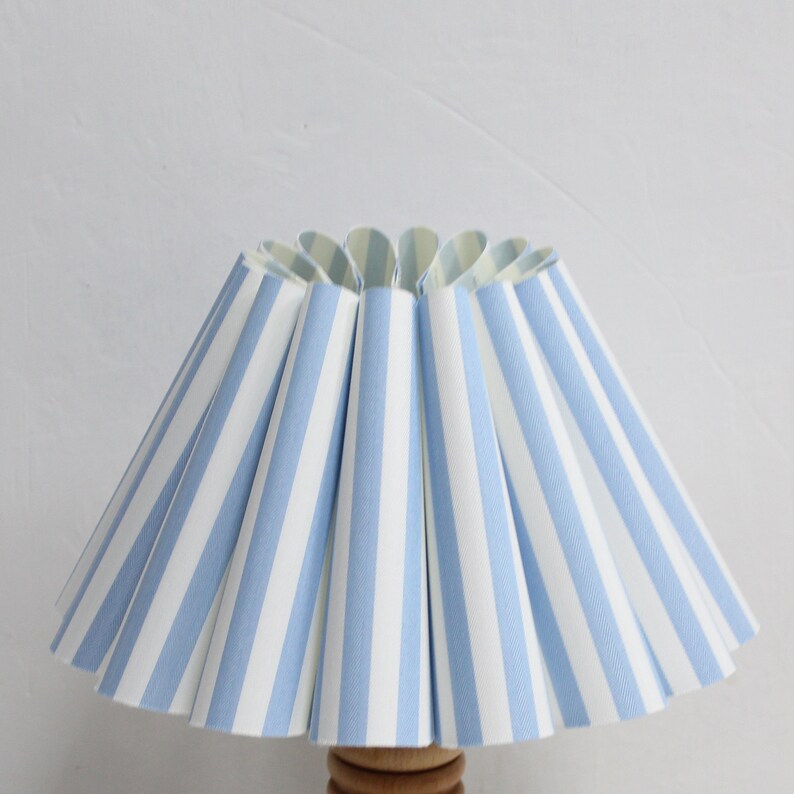 Pu&ograve; includere: Un paralume a righe blu e bianche con un design plissettato.