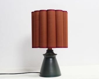 May include: A table lamp with a dark green ceramic base and a pleated brown lampshade with a burgundy trim.