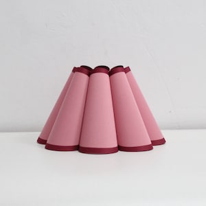 Può includere: Un paralume rosa con un bordo color borgogna, composto da più pannelli a forma di cono.