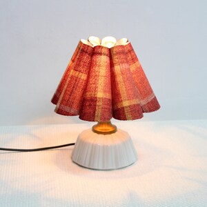 May include: A small table lamp with a white ceramic base and a red and yellow plaid fabric shade.