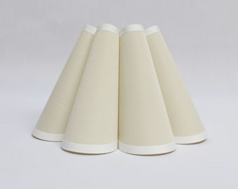 May include: A set of five off-white lampshades with white trim. The lampshades are cone-shaped and have a pleated design.