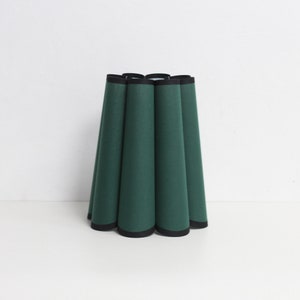 May include: A green lampshade with a black trim. The lampshade is pleated and has a rounded shape.