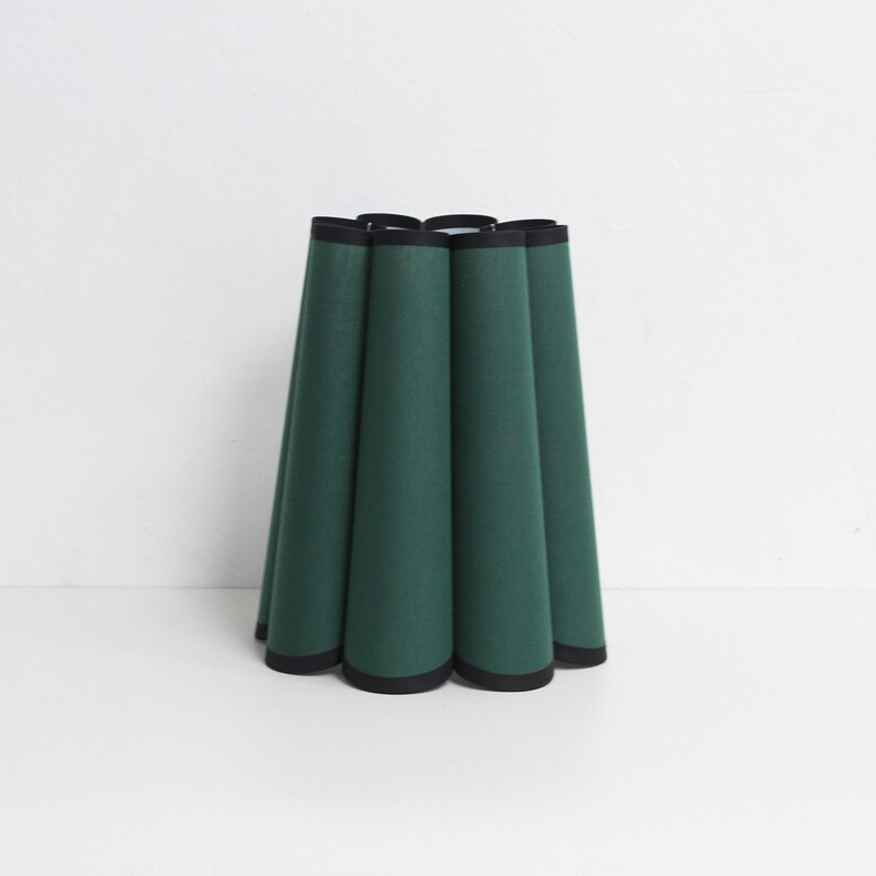 May include: A green lampshade with a black trim. The lampshade is pleated and has a rounded shape.