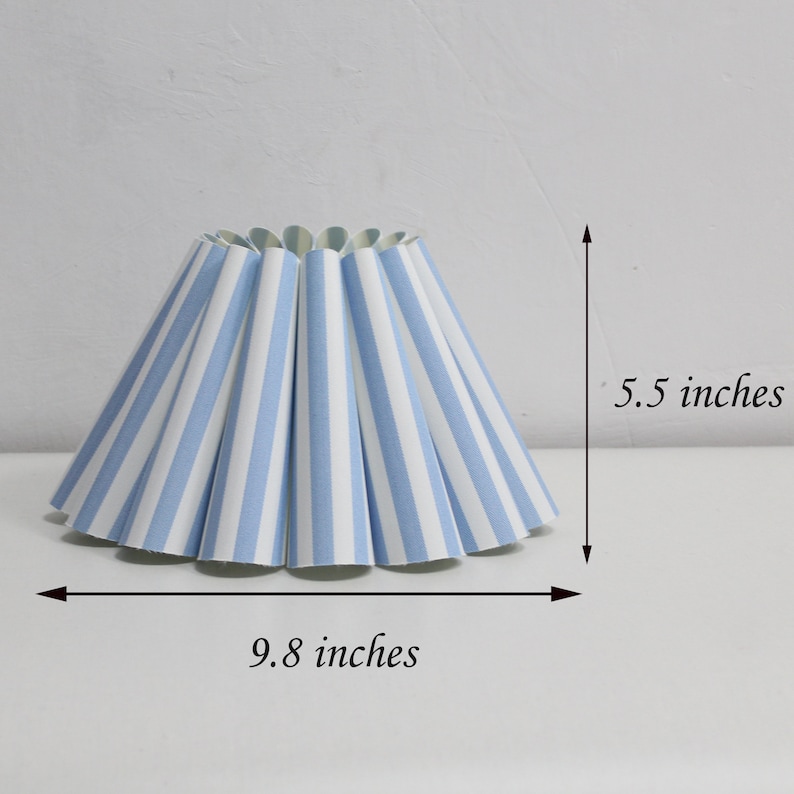 Pu&ograve; includere: Un paralume a righe blu e bianche con un diametro di 25 cm e un'altezza di 14 cm.