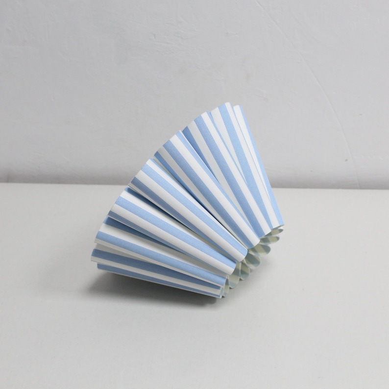 Pu&ograve; includere: Un cono di carta a strisce blu e bianche piegato a forma di ventaglio. Il cono &egrave; fatto di carta e ha uno sfondo bianco con strisce blu.