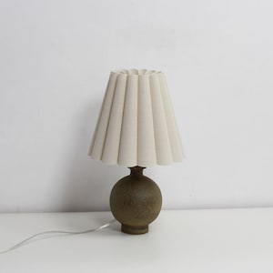 May include: A table lamp with a pleated white fabric shade and a brown ceramic base.