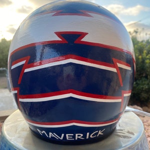 May include: A blue, white, and red painted motorcycle helmet with the word "MAVERICK" written in white on the bottom.