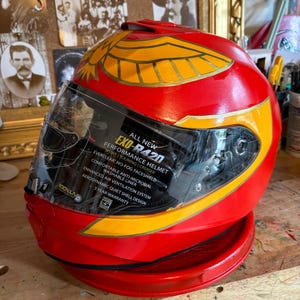 May include: Red motorcycle helmet with a gold eagle design and a clear visor. The helmet has the text "ALL NEW EXO-R420 PERFORMANCE HELMET" on the visor.