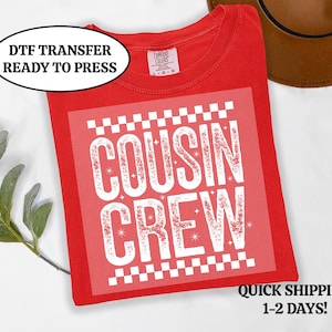 以下が含まれることがあります： 「COUSIN CREW」と書かれた白いグラフィックが特徴の赤いTシャツ。シャツには、黒い楕円の中に「DTF TRANSFER READY TO PRESS」という文字も入っています。シャツは折りたたまれており、すぐに着用できます。