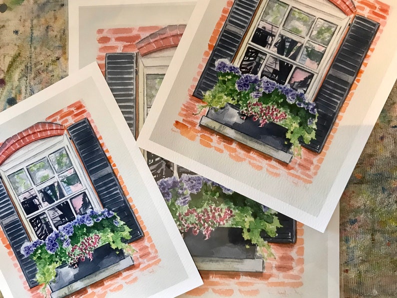 May include: Four watercolor paintings of a brick building with a window and flower box. The window has black shutters and the flower box is filled with purple and red flowers. The paintings are on white paper.