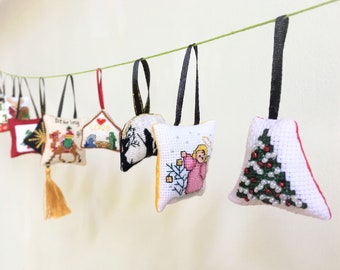 May include: A string of 12 handmade Christmas ornaments, each featuring a different embroidered design. The ornaments are white with colorful embroidery and are hung on a green string. The designs include a Christmas tree, a star, an angel, and a nativity scene.