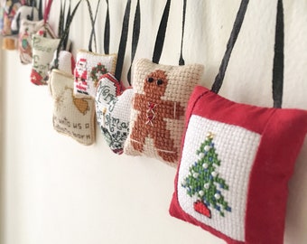 May include: A string of small, handmade Christmas ornaments with various designs, including a gingerbread man, a Christmas tree, and a Santa Claus. The ornaments are made of fabric and are decorated with cross-stitch embroidery.