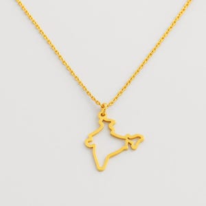 May include: A gold-colored necklace featuring a pendant in the shape of the map of India. The pendant is a simple outline of the country's borders, suspended from a delicate chain. The necklace is displayed against a plain white background.