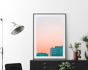 May include: A framed photograph of a city skyline at sunset. The buildings are a teal blue color and the sky is a soft pink and orange.
