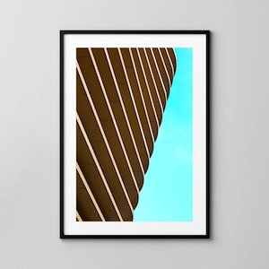 May include: A close-up of a building with a curved facade. The building is made of brown and white horizontal panels, creating a striped pattern. The sky is a bright blue.