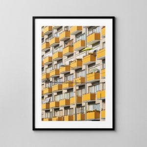 Puede incluir: Una fotografía de un edificio de apartamentos amarillo y blanco con balcones. Los balcones están bordeados de plantas y algunos tienen sombrillas.