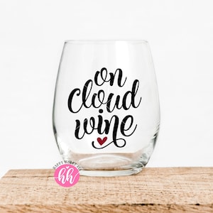 Op de afbeelding: Een helder glazen wijnglas met de tekst "on cloud wine" in zwarte schrijfletters met een klein rood hartje onder het woord "wine".