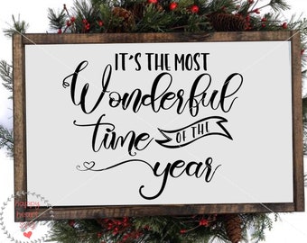 May include: A white wooden sign with black text that reads "It's the most wonderful time of the year". The sign is framed with a dark brown wood frame.