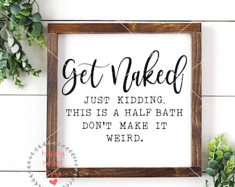 May include: A white sign with a brown wooden frame, featuring the text "Get Naked" in a cursive font. The text "Just Kidding, This is a Half Bath Don't Make It Weird." is printed in a black sans-serif font below the main text.