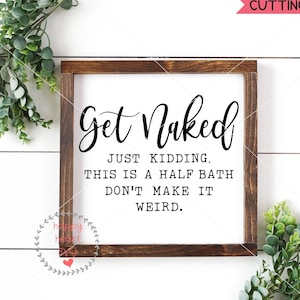 May include: A white sign with a brown wooden frame, featuring the text "Get Naked" in a cursive font. The text "Just Kidding, This is a Half Bath Don't Make It Weird." is printed in a black sans-serif font below the main text.
