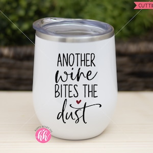May include: White wine tumbler with black text that reads "Another wine bites the dust" with a small red heart above the word "dust".