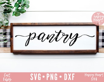 Op de afbeelding: Een wit houten bord met een bruin frame, waarop het woord "pantry" in zwarte cursieve letters staat. Het bord is geplaatst op een witte houten achtergrond met zwart-wit geblokt lint.
