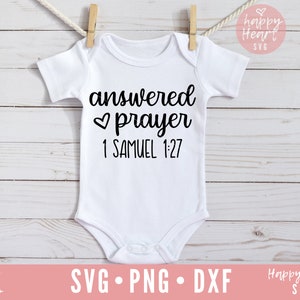 Op de afbeelding: Witte baby romper met zwarte tekst die "answered prayer 1 Samuel 1:27" luidt, met een klein hartje symbool voor het woord "prayer".