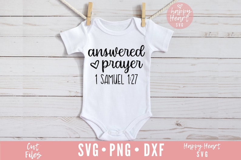 Op de afbeelding: Witte baby romper met zwarte tekst die "answered prayer 1 Samuel 1:27" luidt, met een klein hartje symbool voor het woord "prayer".