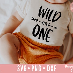 K&ouml;nnte beinhalten: Ein Baby tr&auml;gt einen wei&szlig;en Strampler mit dem Text "WILD and ONE" in schwarzen Buchstaben und einer Pfeilgrafik. Das Baby tr&auml;gt eine orangefarbene Hose und liegt auf einer wei&szlig;en Oberfl&auml;che.