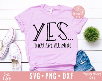 Könnte beinhalten: Ein pinkfarbenes T-Shirt mit dem Text "YES... THEY ARE ALL MINE" in schwarzer Schrift. Das Shirt liegt auf einem weißen Holzgrund mit einem Paar weißen Turnschuhen, einer kleinen Topfpflanze und einer blauen Jeans-Shorts.